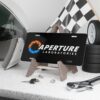 aperture-laboratories-decorative-vanity-license-plate-black-background-display-mockup Aperture Laboratories novelty license plate black background shown as a display piece, science laboratory vanity car tag. Inspired by Portal.